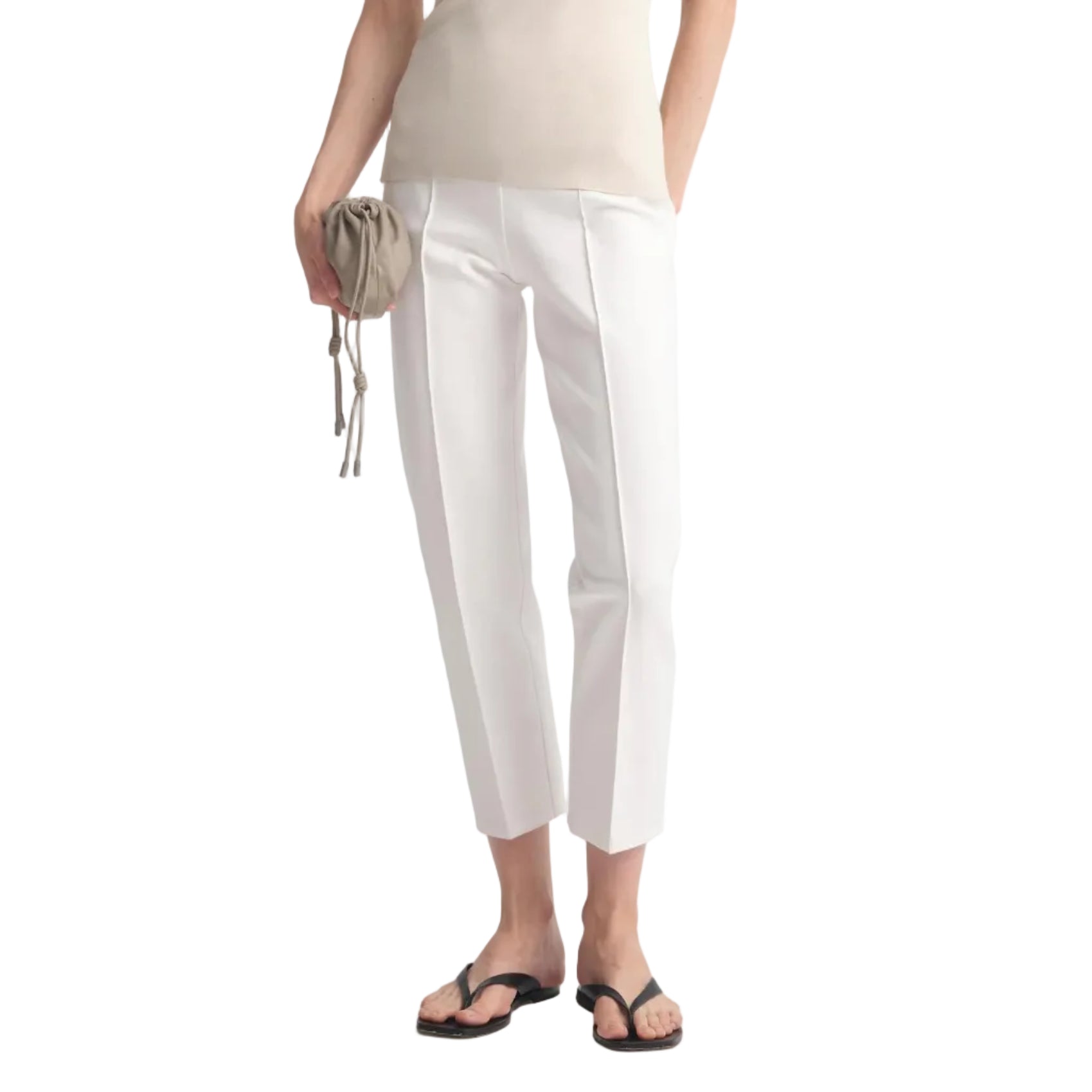 A woman modeling a light beige ribbed tank top and white cropped trousers, holding a small beige clutch, against a light gray studio background.